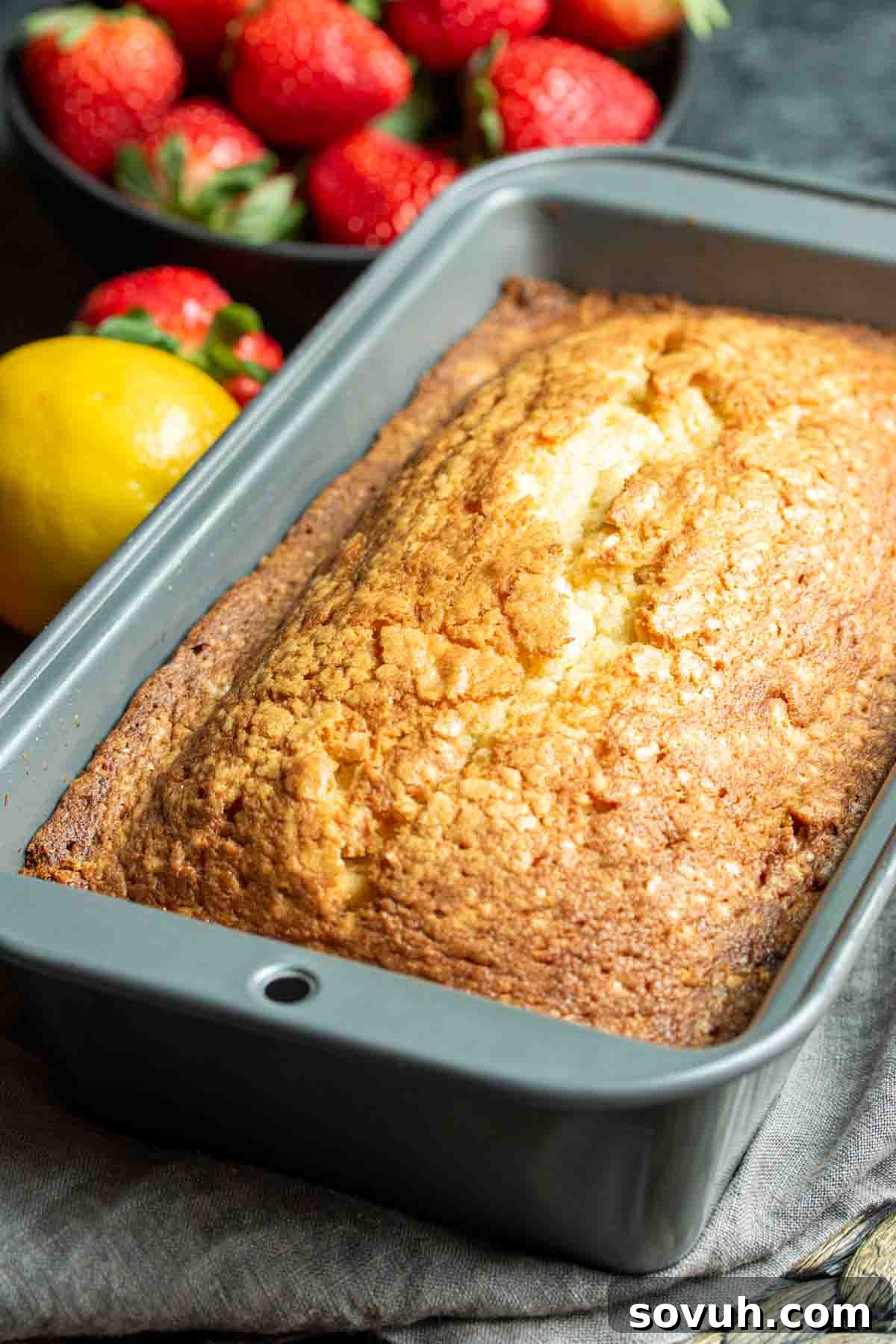 A golden brown loaf of lemon bread cooling in a pan, garnished with fresh strawberries.