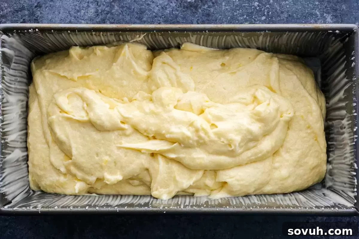 A freshly baked lemon loaf cake cooling in its pan, showing a perfectly golden-brown crust.