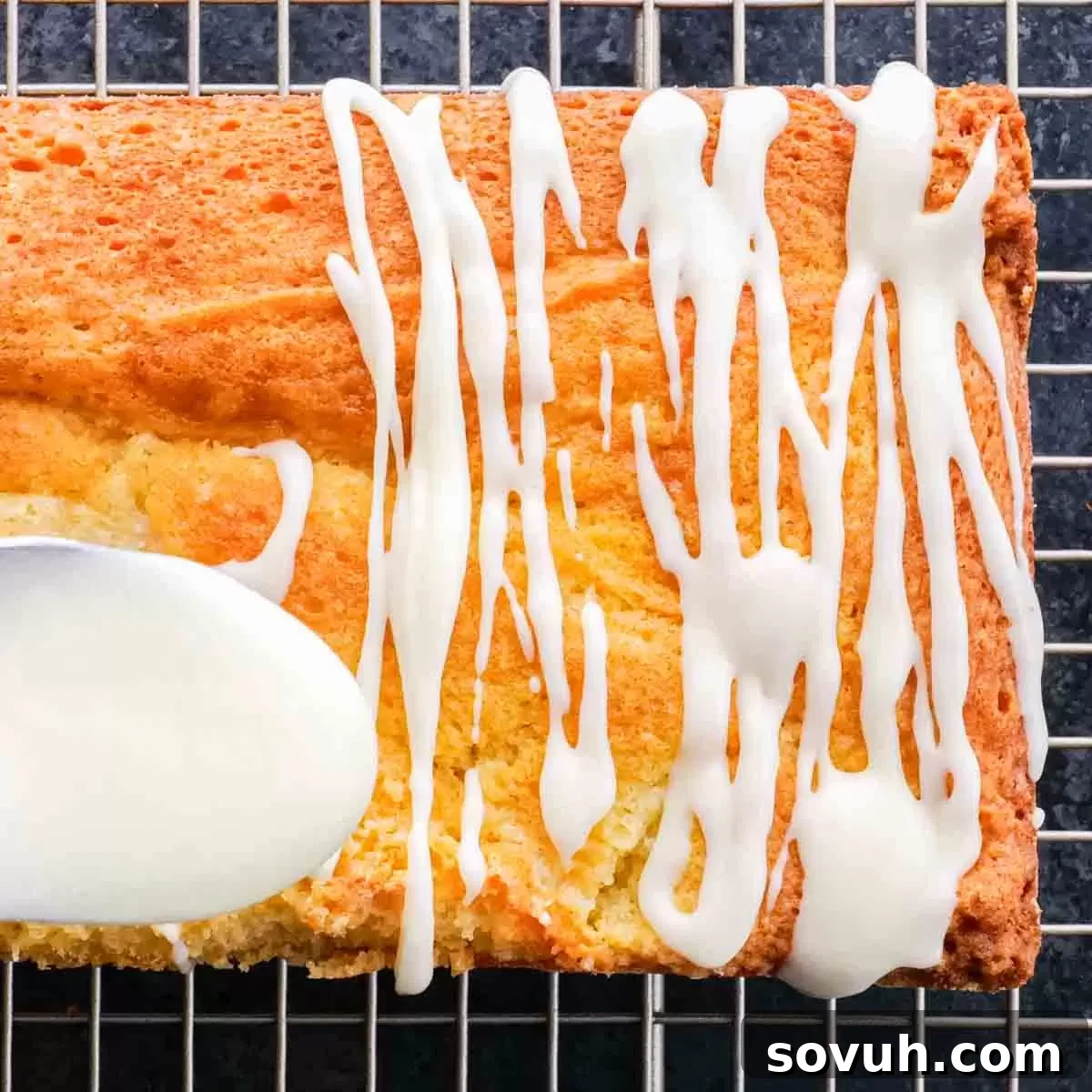 A lemon loaf cake with a generous lemon icing and a spoon resting on a cooling rack, glistening and ready.