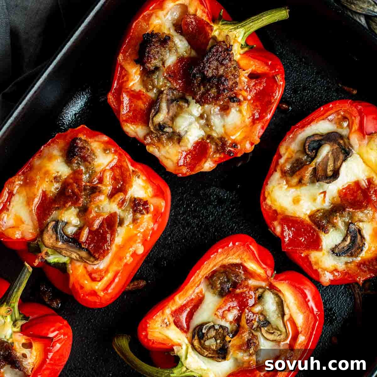 Red bell pepper halves stuffed with mushrooms, meat, and melted cheese arranged on a black tray. Highlighting a healthy and delicious low-carb pizza alternative.