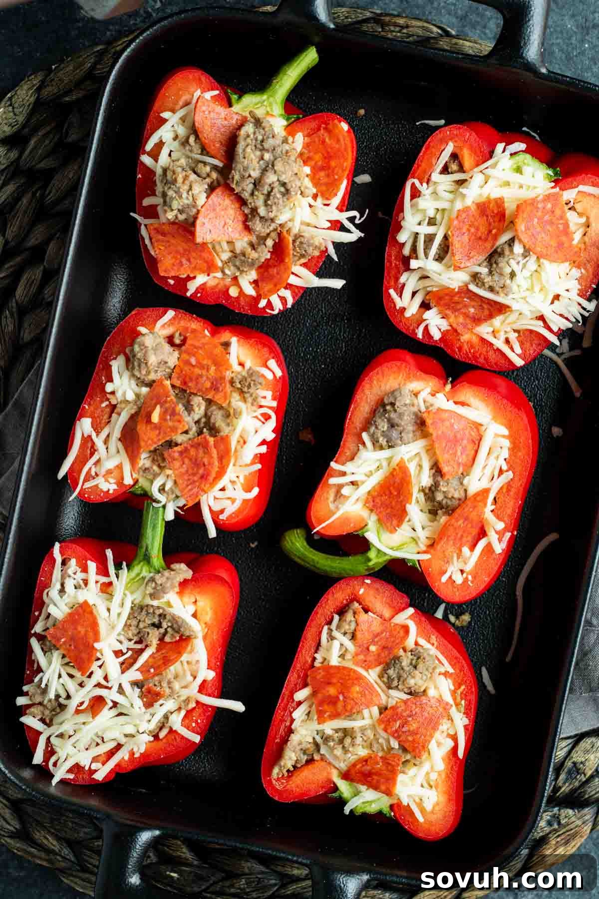 Red bell peppers stuffed with ground meat, shredded cheese, and pepperoni slices, arranged in a black baking dish, ready to be baked to golden perfection.