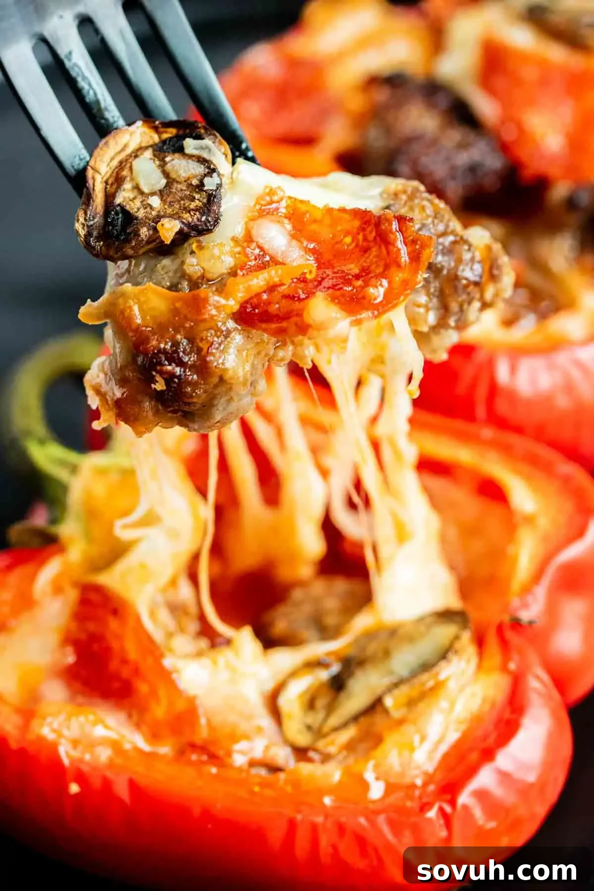 A fork lifts a cheesy, stuffed red bell pepper half, revealing melted cheese, mushrooms, pepperoni, and sausage, ready to be enjoyed.