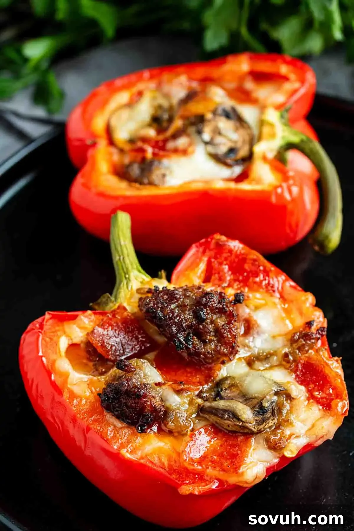 Two red bell pepper halves on a plate, filled with melted cheese, mushrooms, and sausage, garnished with fresh herbs, ready to be served.
