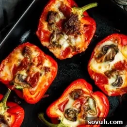 Red bell pepper halves stuffed with mushrooms, meat, and melted cheese arranged on a black tray.