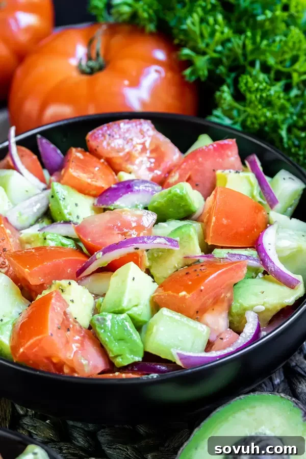 A serving of Cucumber Tomato Avocado Salad on a plate, garnished with fresh herbs.