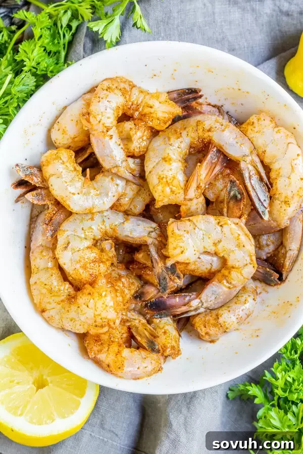 Raw shrimp being seasoned with Old Bay and oil in a bowl