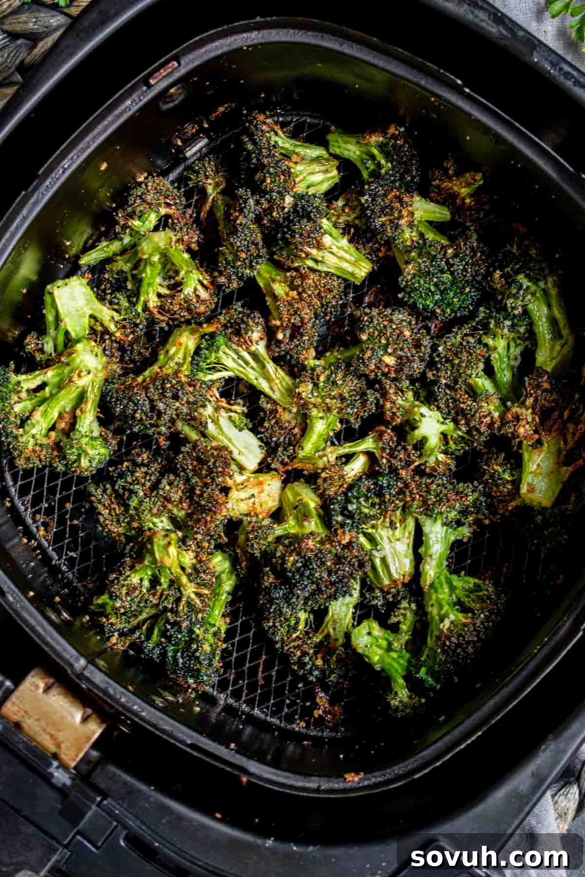 Air Fryer Broccoli florets cooking in an air fryer basket, showing early stages of crisping.