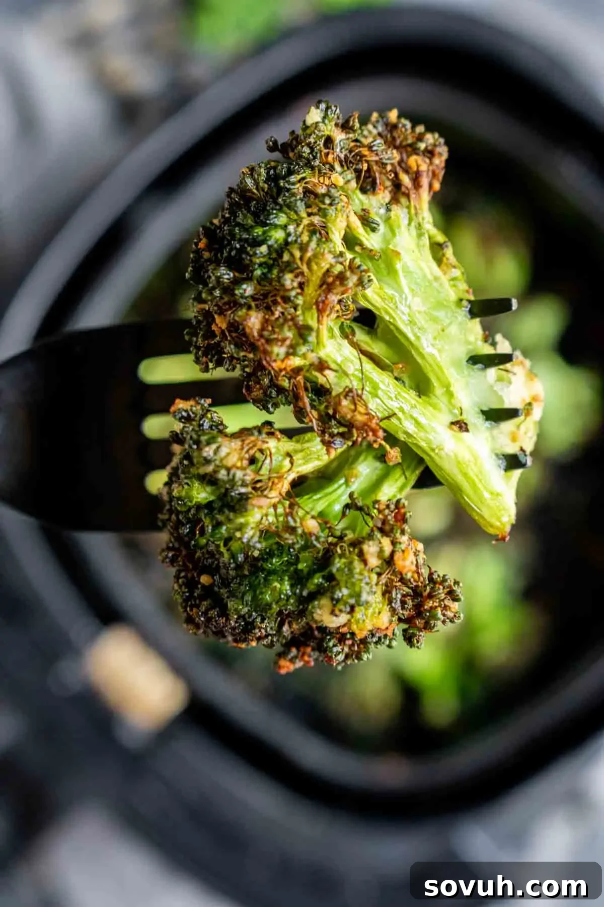 A single air fryer broccoli floret held by tongs, showcasing its crispy, charred edges and tender interior.