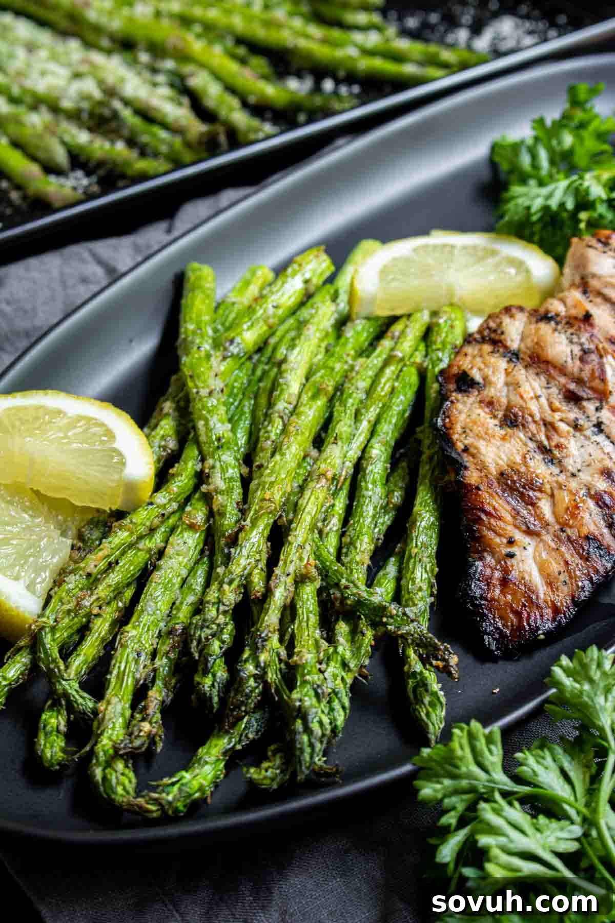 Grilled chicken breast with lemon and a side of Air Fryer Asparagus on a black plate.