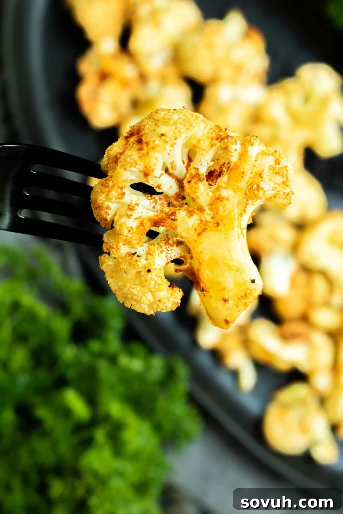 Crispy Air-Fried Cauliflower Bites 5 A perfectly roasted piece of air fryer cauliflower on a fork, held over a white plate, seasoned with flavorful spices.
