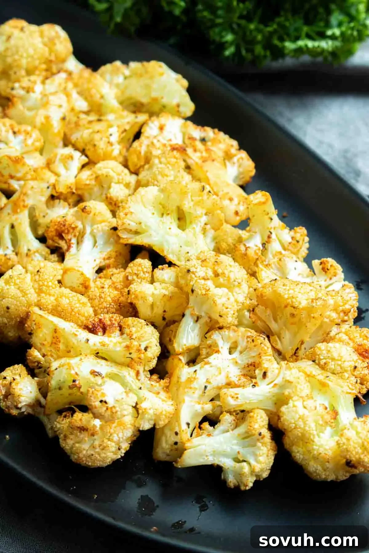 Crispy Air-Fried Cauliflower Bites 6 A black plate filled with perfectly roasted and crispy air fryer cauliflower florets, ready to be enjoyed as a delicious and healthy meal.