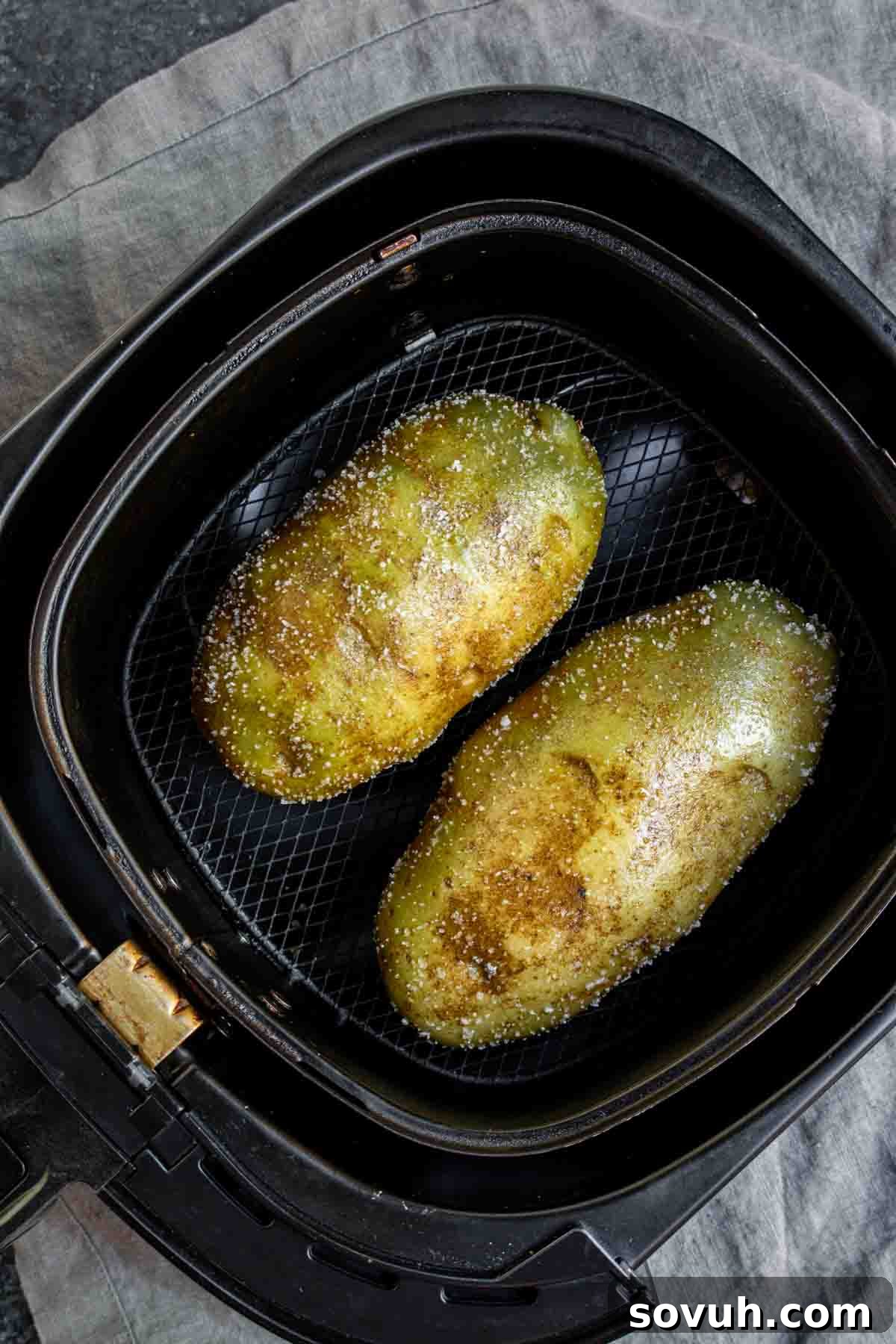 Two seasoned Air Fryer Baked Potatoes in an air fryer basket.