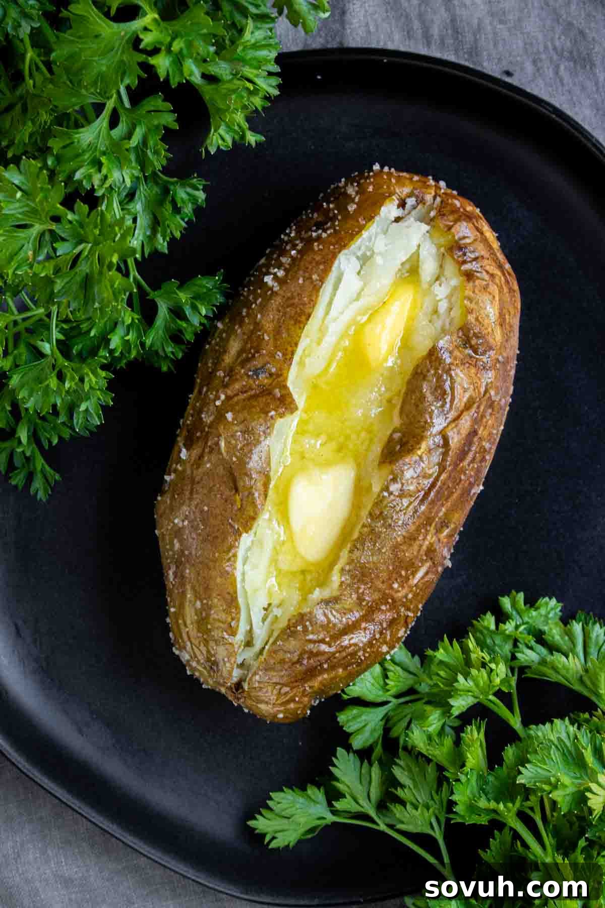 Air Fryer Baked Potato with melting butter on a black plate garnished with fresh parsley.