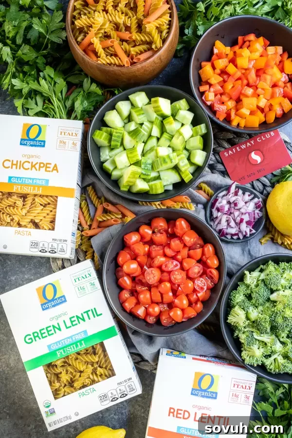 A collection of fresh ingredients laid out for making vegan pasta salad, including gluten-free pasta, sliced vegetables, and herbs.