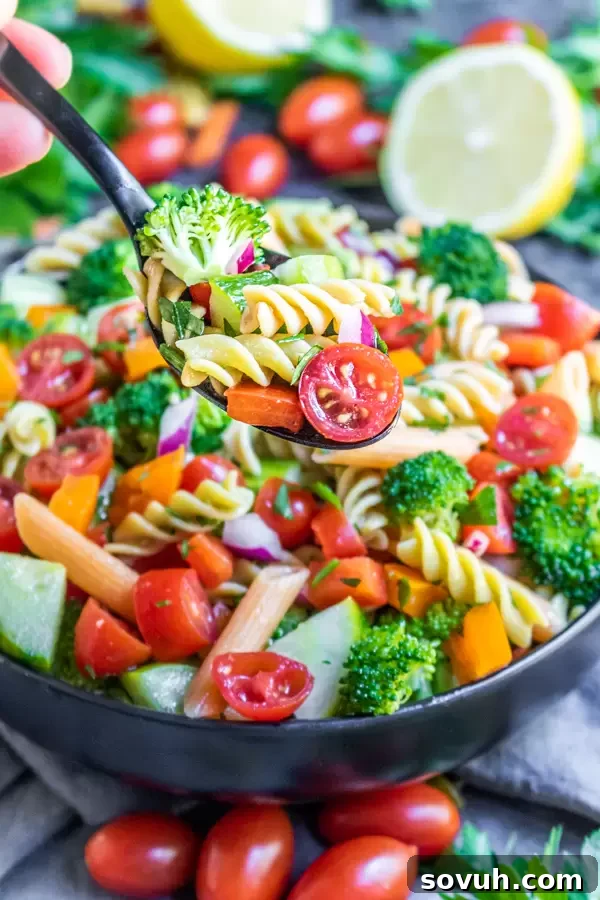 A hand scooping a serving of vegan pasta salad from a large bowl, highlighting its freshness and vibrant ingredients.