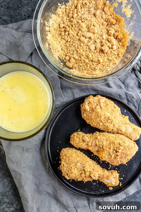 Close-up view of chicken pieces being coated in a seasoned keto-friendly batter of crushed pork rinds and almond flour, preparing them for the air fryer.