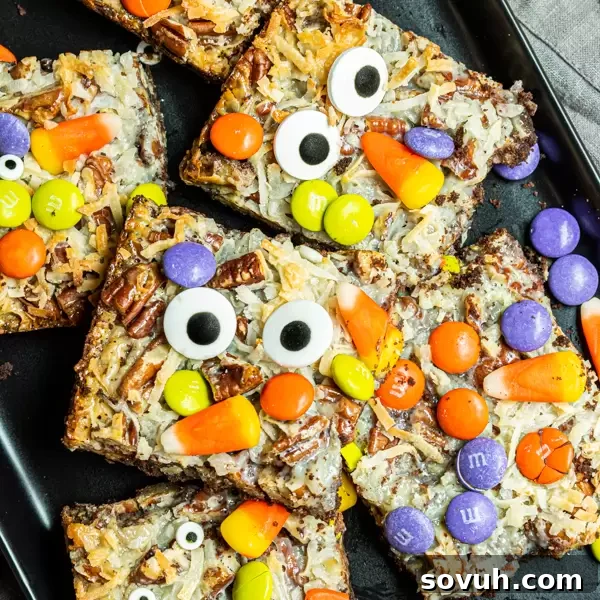 A plate of freshly baked Halloween Magic Cookie Bars, showing their distinct layers of chocolate crust, nuts, coconut, and colorful M&Ms and candy corn.