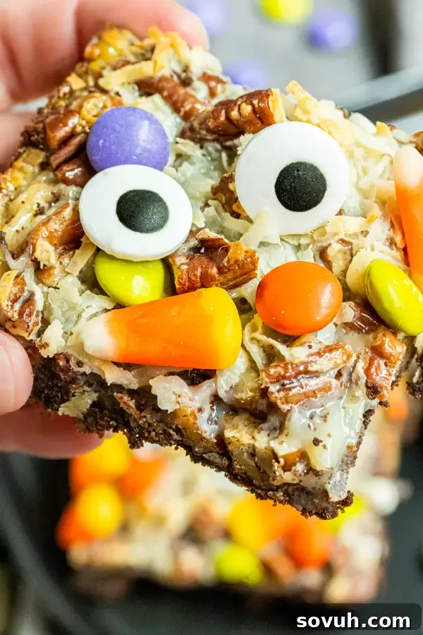 A hand holding a single Halloween Magic Cookie Bar, showing off its generous layers of candy and gooey texture.