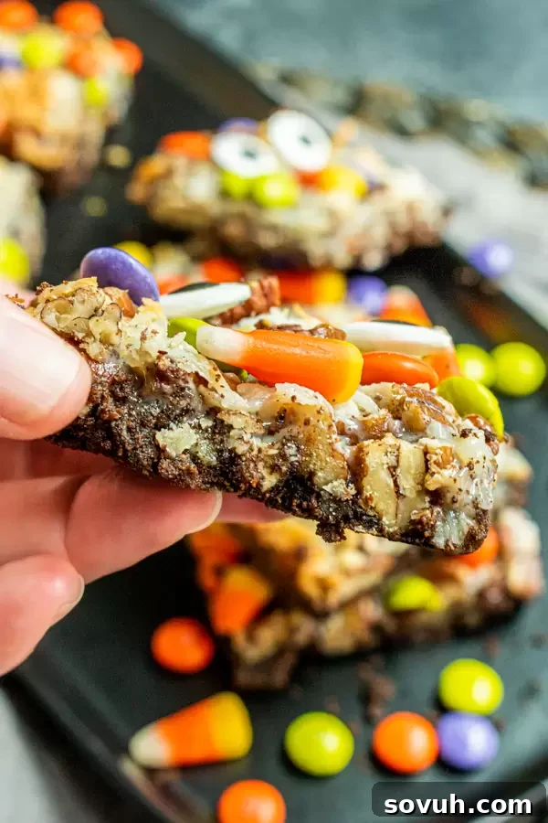 Another close-up of a hand holding a Halloween Magic Cookie Bar, emphasizing its delightful texture and festive candy toppings.