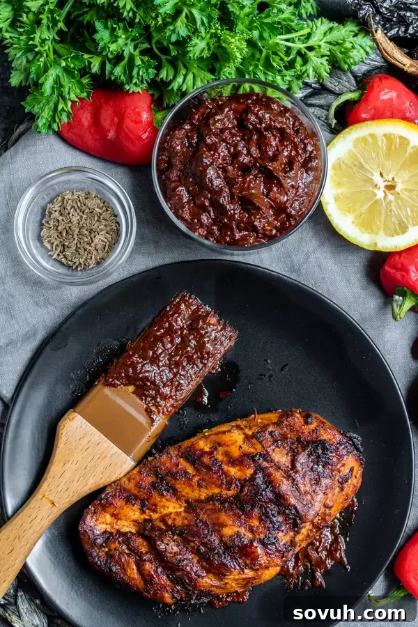 An inviting overhead shot of a bowl of Harissa Paste next to plates of Harissa-coated chicken, emphasizing the meal potential.