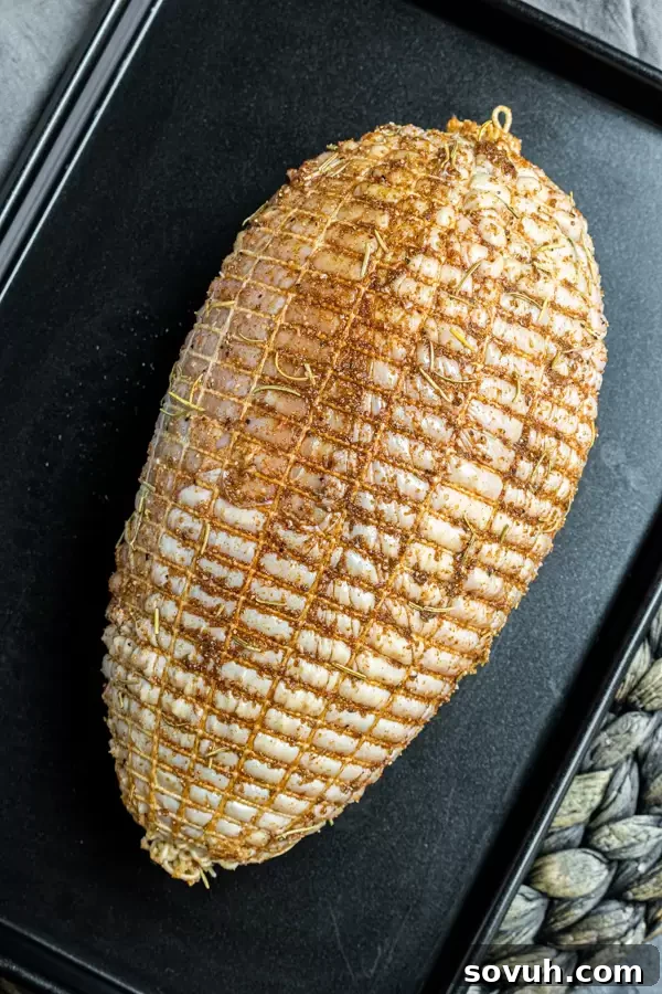 A boneless turkey breast, expertly seasoned with a blend of herbs and spices, tied with butcher's twine, resting on a sheet pan ready for cooking.