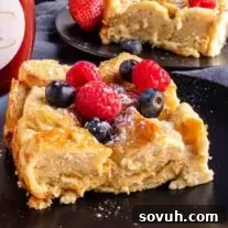 A slice of Overnight French Toast Bake with berries and syrup on a black plate.
