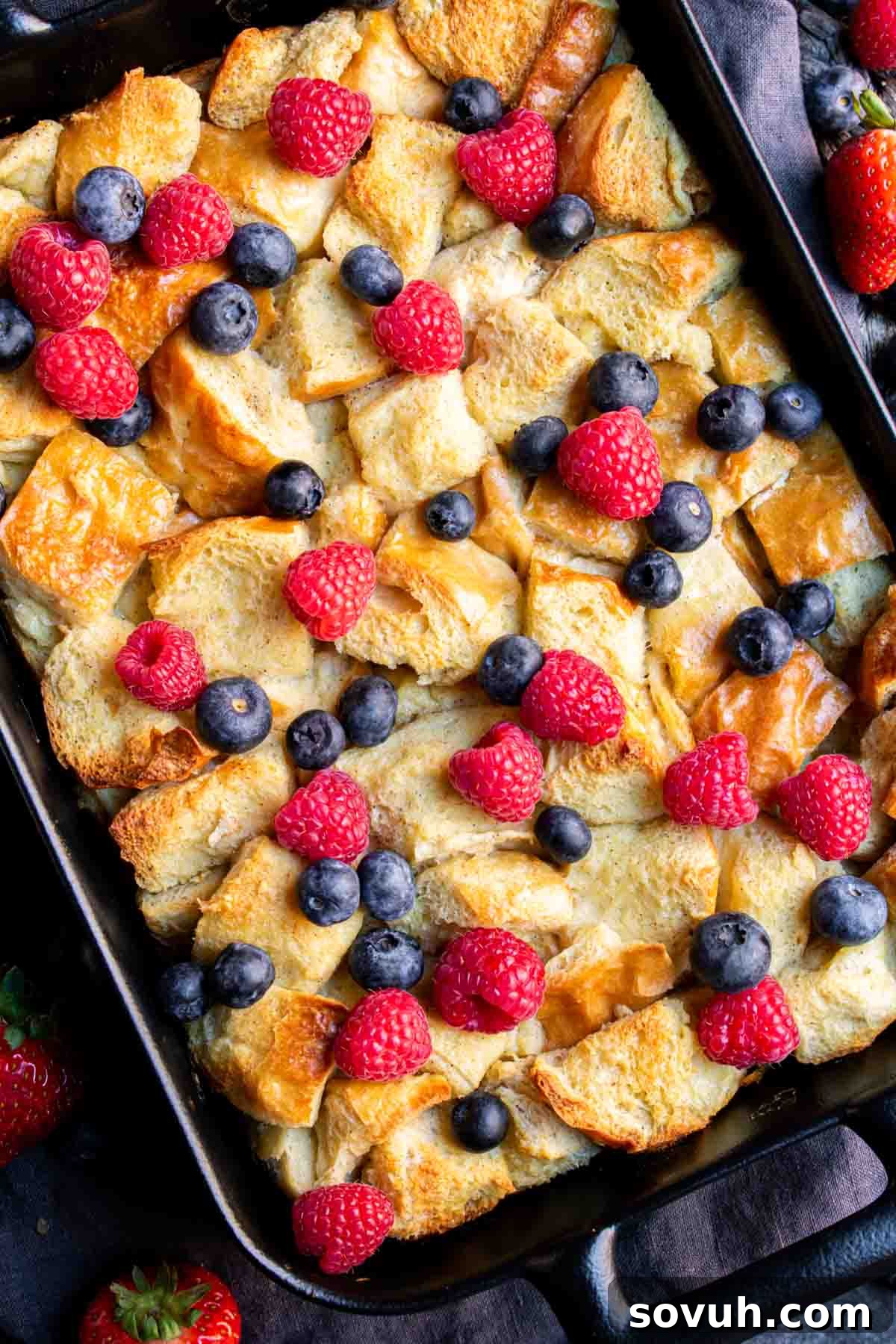 A tantalizing view of an Overnight French Toast Bake, overflowing with fresh berries and blueberries, presented in a black cast iron pan, ready to be served.