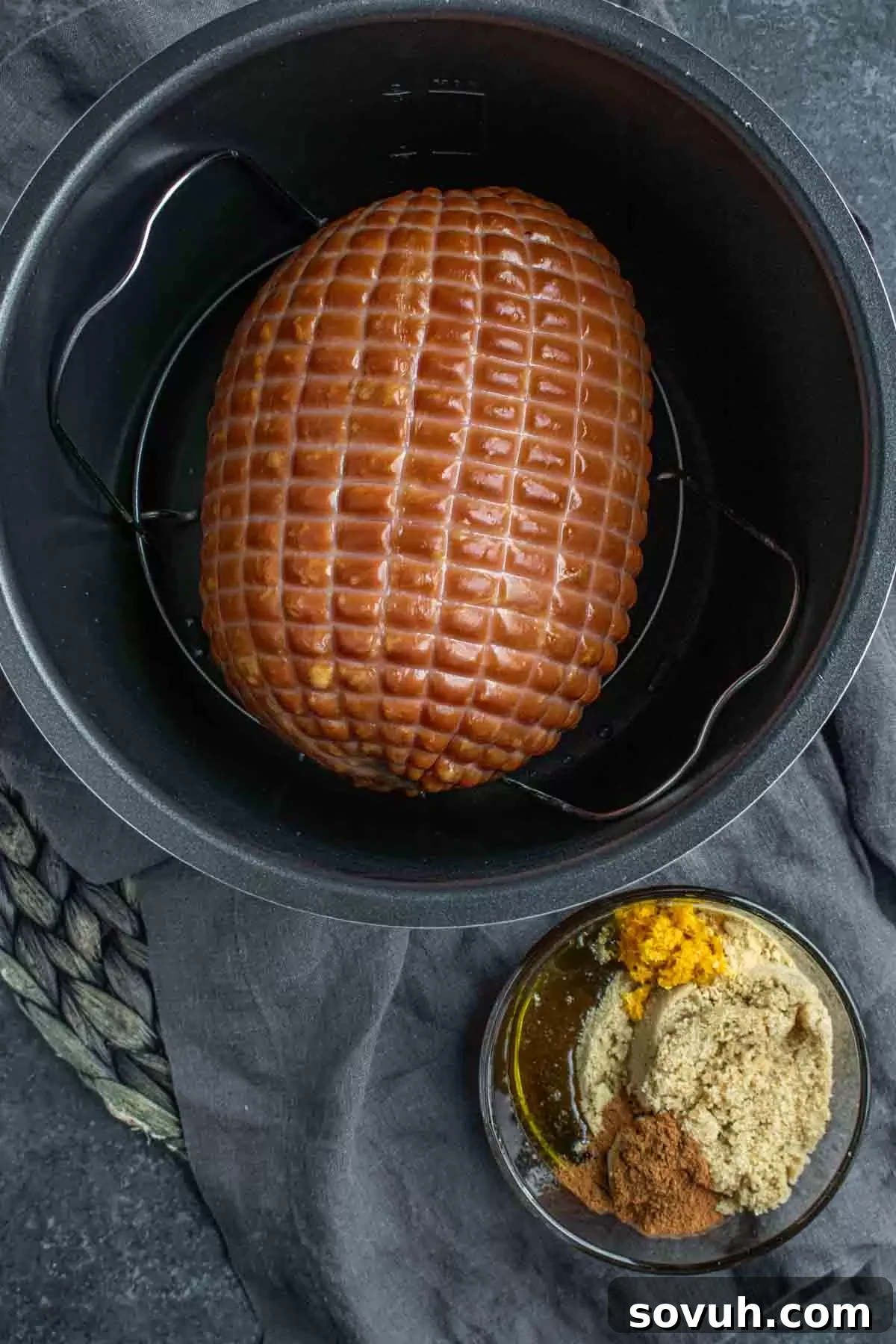 A whole, netted ham prepared for cooking, resting next to a bowl of brown sugar, ground ginger, cinnamon, and fresh orange zest—key ingredients for a delicious Instant Pot ham glaze.