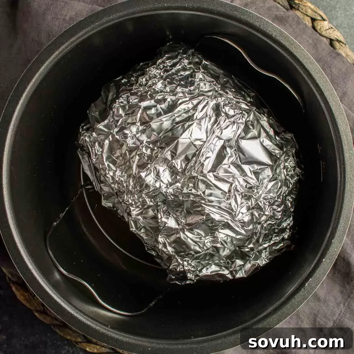 A round ham, securely wrapped in aluminum foil, is placed inside a black pressure cooker on a metal trivet, showcasing the setup for an easy ham recipe.