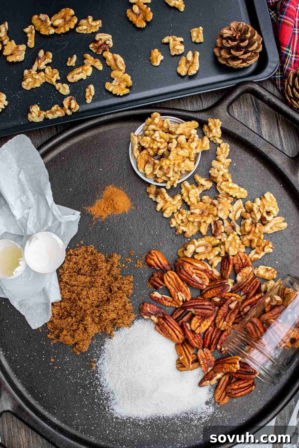A collection of ingredients for candied nuts, including egg, sugars, cinnamon, and mixed pecans and walnuts, laid out on a white surface.
