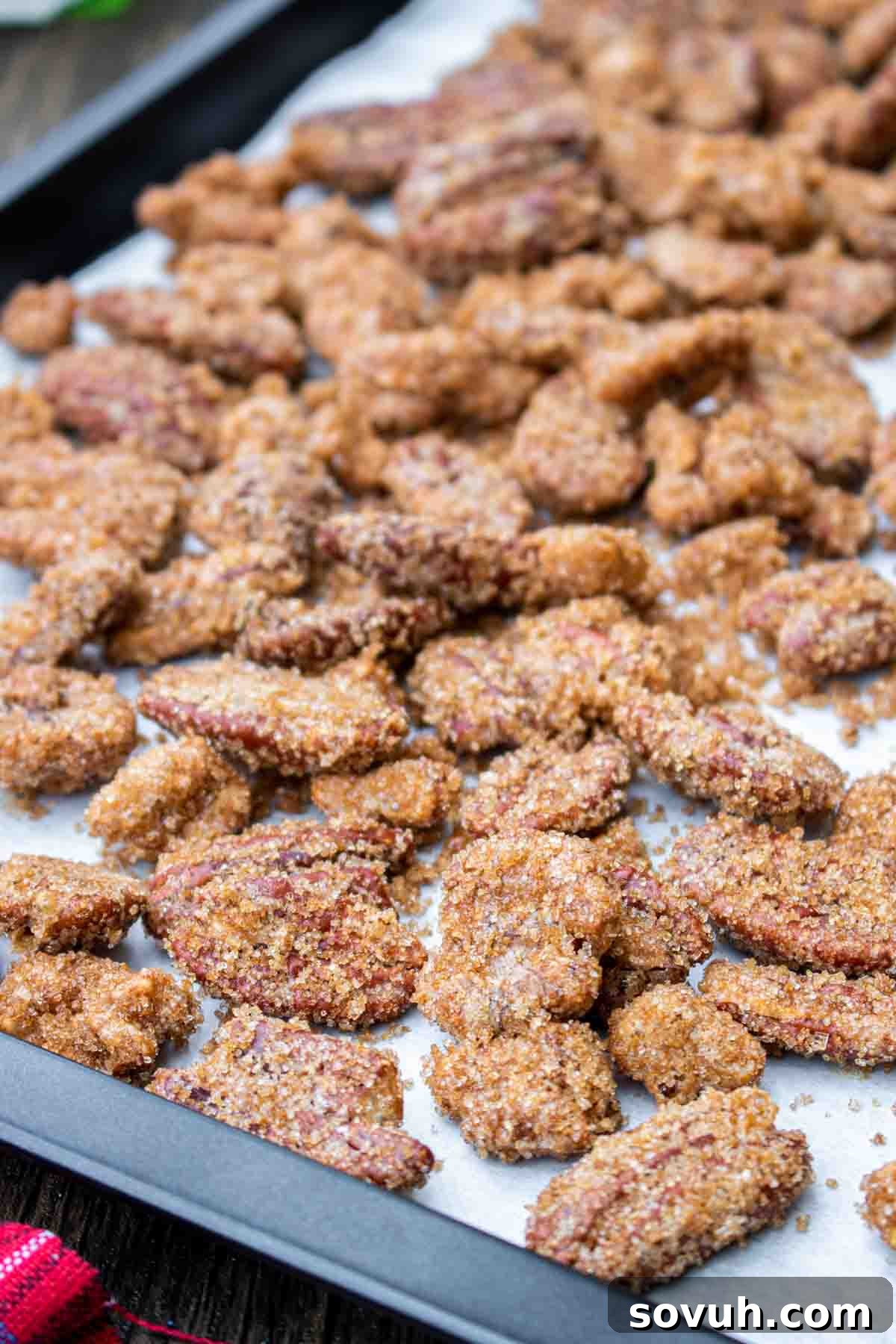 Freshly baked candied nuts cooling on a black sheet pan lined with parchment paper, perfectly golden and crispy.