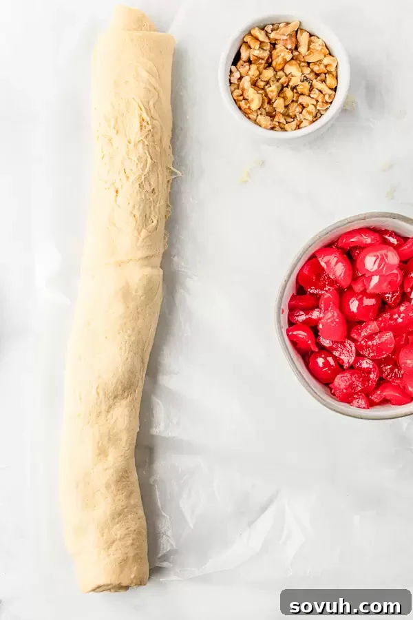 A rolled-up crescent dough log filled with a creamy mixture, visible maraschino cherries and chopped nuts peeking out.