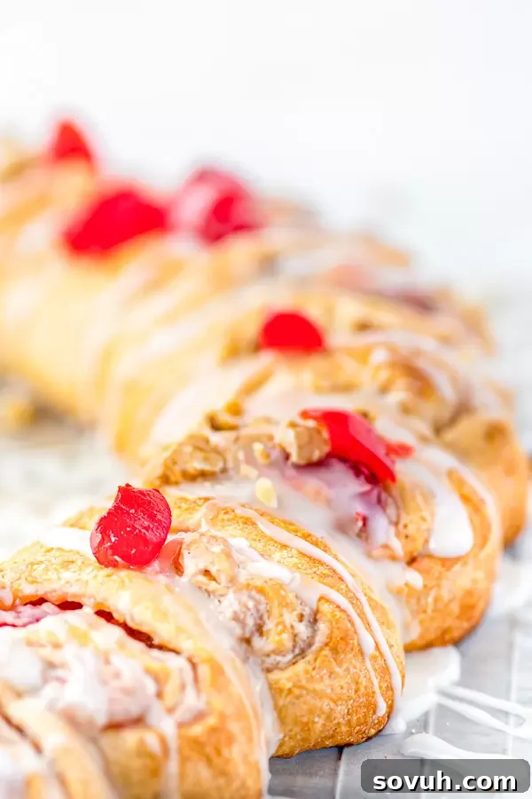 A close-up of a slice of Holiday Crescent Ring, showing the luscious cream cheese and cherry filling, topped with icing.
