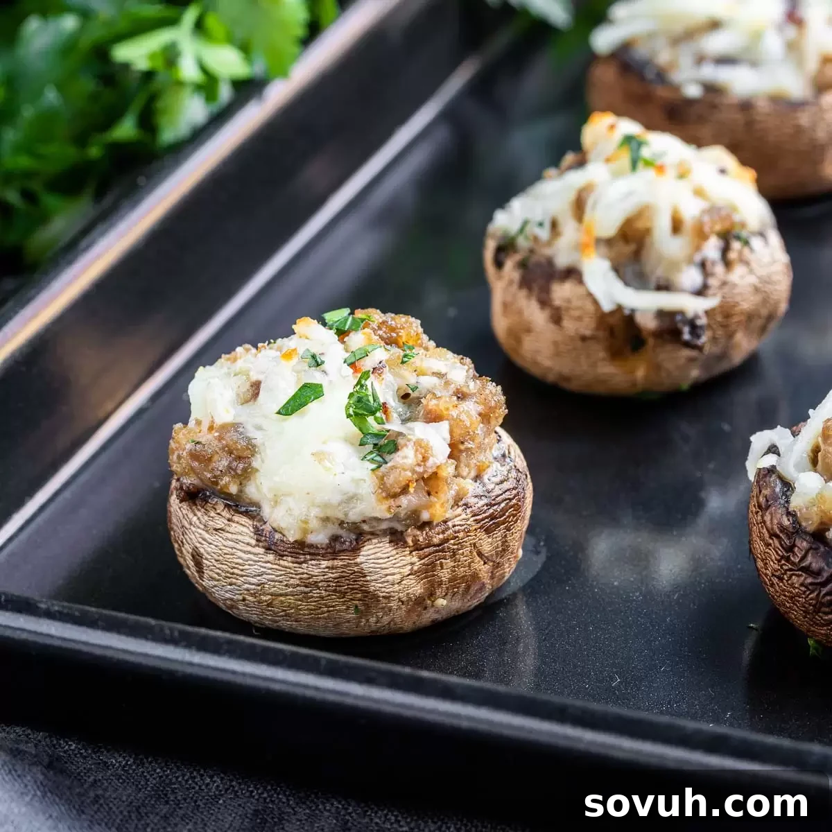 Stuffed mushrooms with sausage on a black baking sheet, ready for serving. Perfect keto party appetizer.