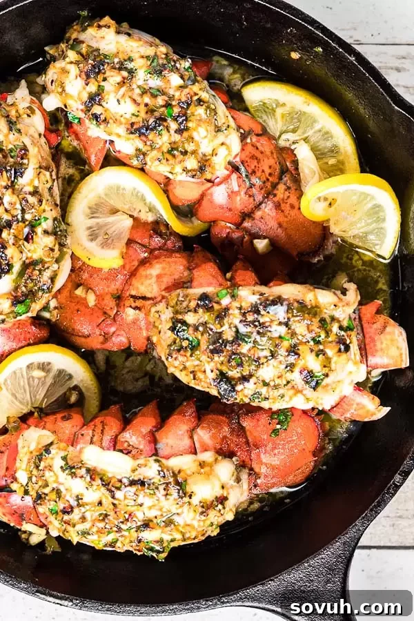 Broiled Lobster Tail in a cast iron skillet with melted herb butter, garnished with fresh herbs and lemon, ready to serve