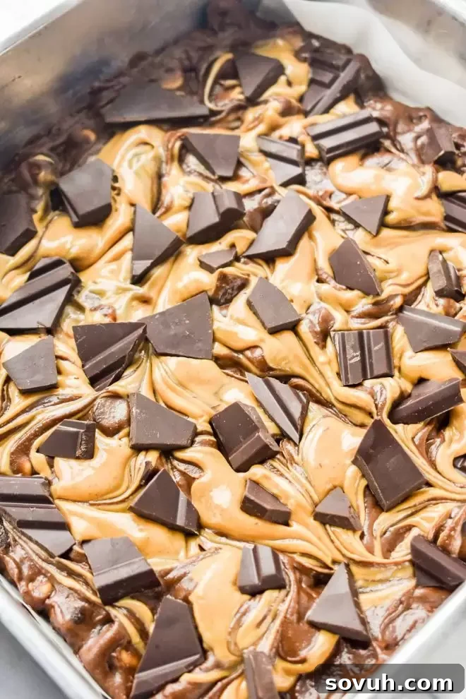 Crushed pieces of high-quality dark chocolate scattered over Dark Chocolate Peanut Butter Brownies before baking.