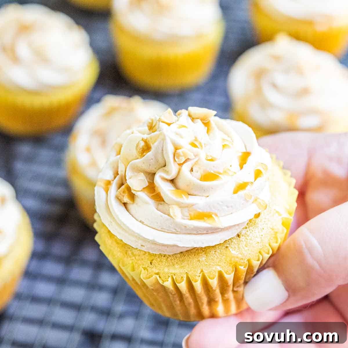 Hand holding frosted caramel apple cupcakes with a drizzle of caramel sauce