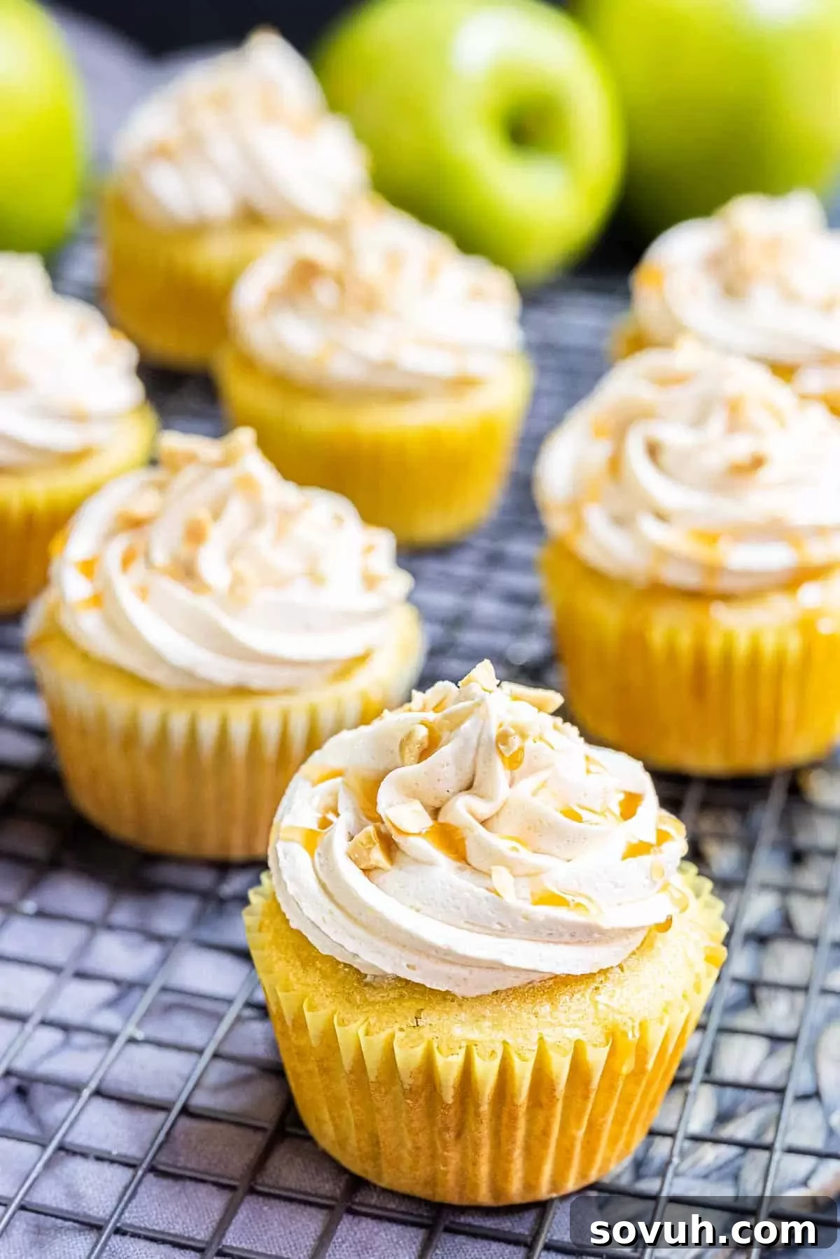 Close-up of a frosted caramel apple cupcake with a drizzle of caramel sauce and a small apple slice garnish