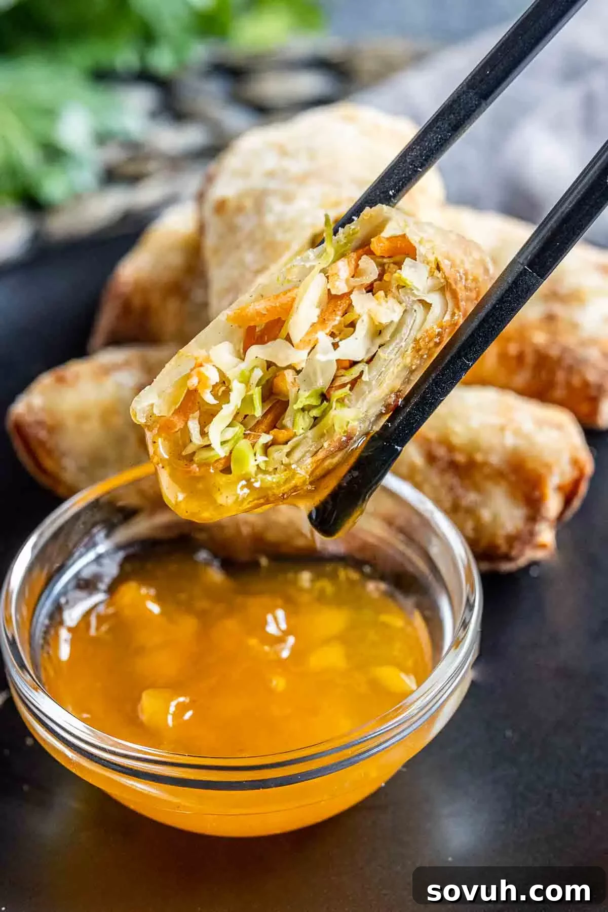 Chopsticks holding an Air Fryer Egg Roll, dipping it into a bowl of duck sauce.