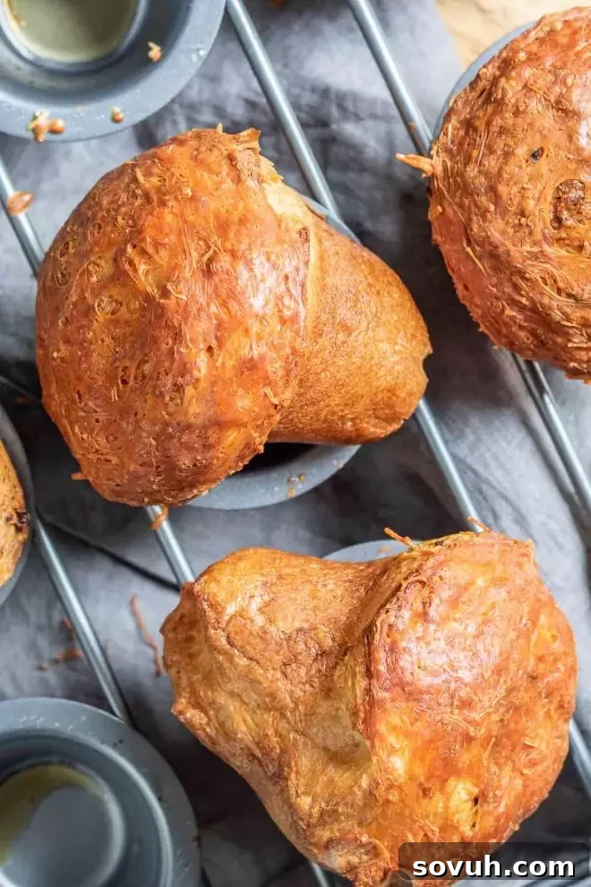 Two freshly baked Garlic Parmesan Popovers resting on the popover pan, showcasing their impressive rise and golden-brown crust.