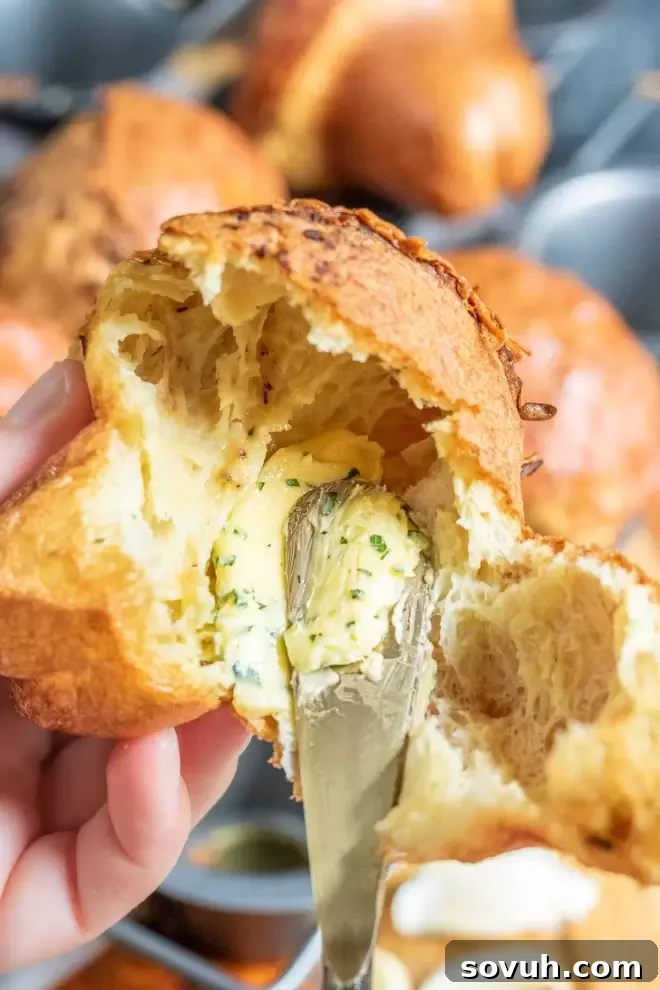 A hand gently brushing a Garlic Parmesan Popover with melted garlic butter, emphasizing its rich flavor and golden appearance.