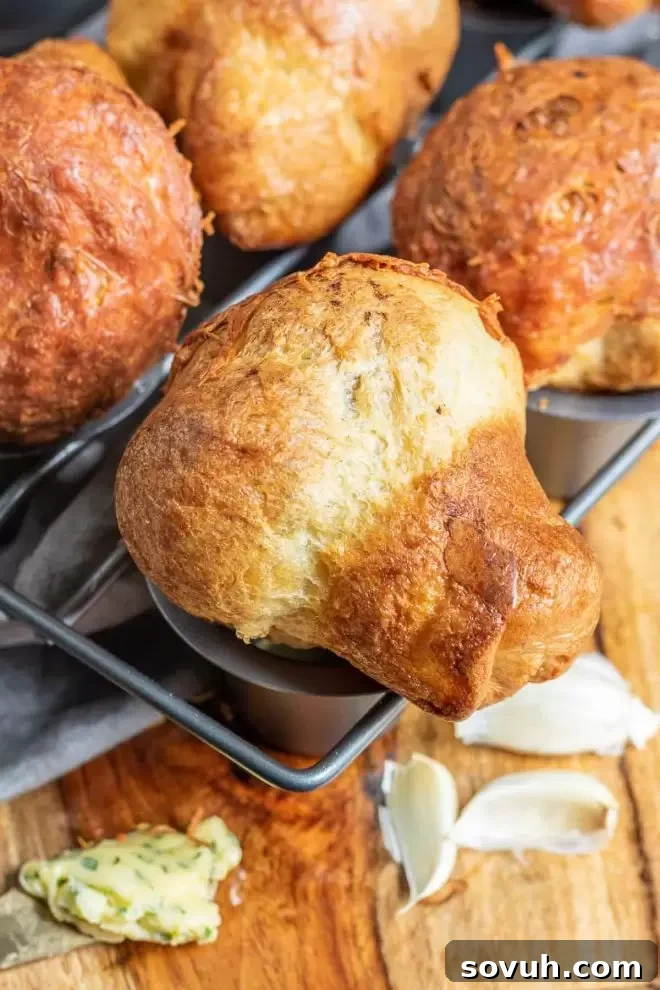 A row of beautifully golden-brown Garlic Parmesan Popovers lying sideways, showcasing their fluffy texture and delicious crust.