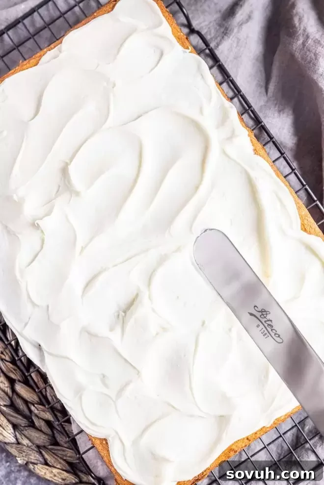 A Coconut Sheet Cake being frosted generously with creamy white icing.