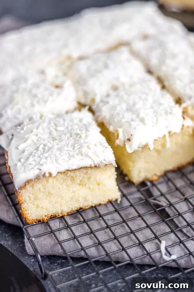 A freshly baked Coconut Sheet Cake, sliced and cooling on a wire rack.