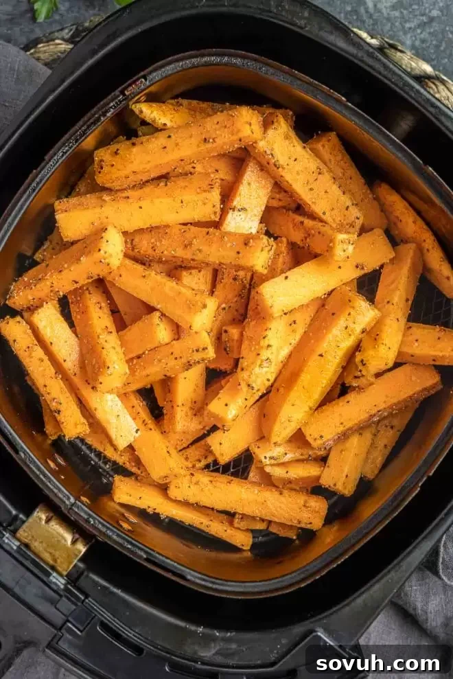 Raw, seasoned sweet potato fries in an air fryer basket, ready to cook.
