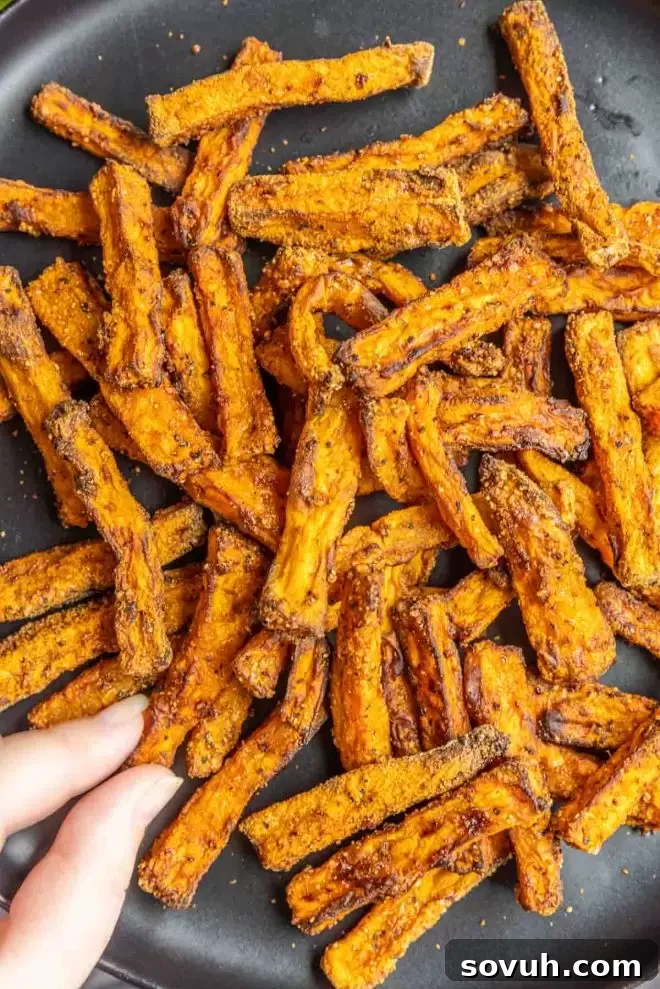 A hand reaching for a crispy Air Fryer Sweet Potato Fry from a plate.