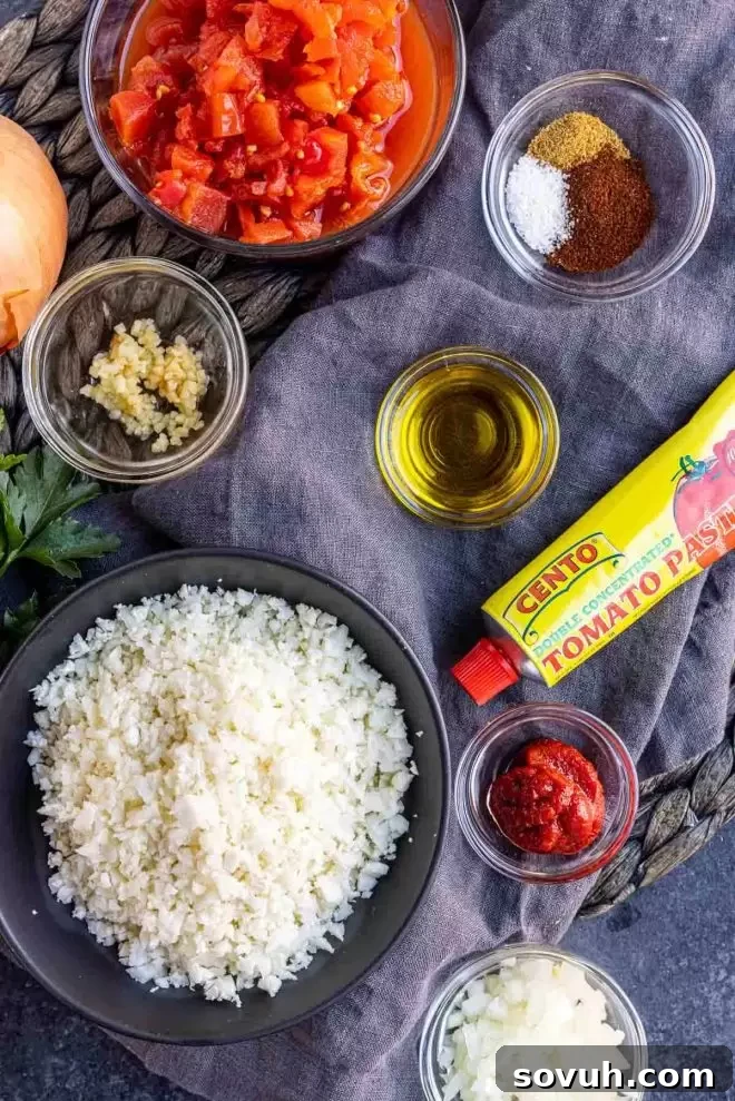 Spanish Fiesta Keto Cauliflower Rice 3 A flat lay photograph showcasing all the fresh and pantry ingredients required to prepare the Keto Cauliflower Spanish Rice, including olive oil, diced onion, minced garlic, Rotel, tomato paste, chili powder, cumin, salt, and cauliflower rice.