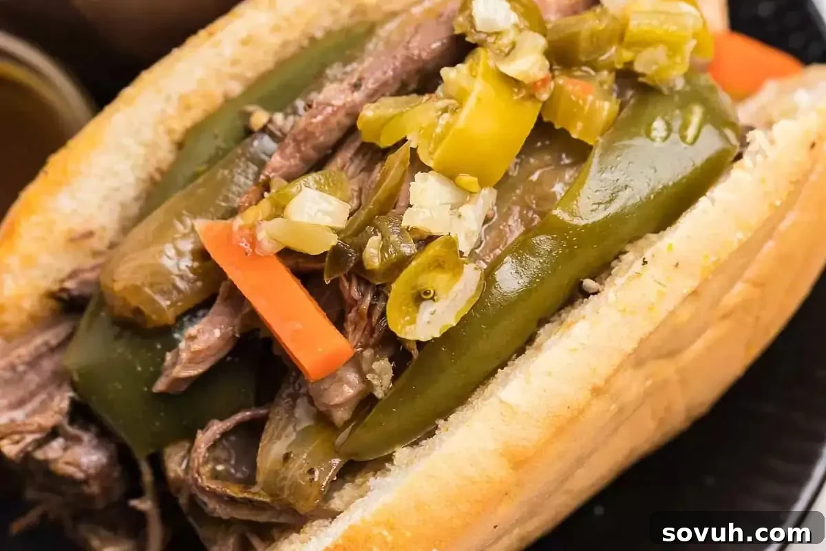 A close-up of an Italian beef sandwich topped with bright green peppers, thinly sliced carrots, and chopped pickles on a soft, crusty bun.