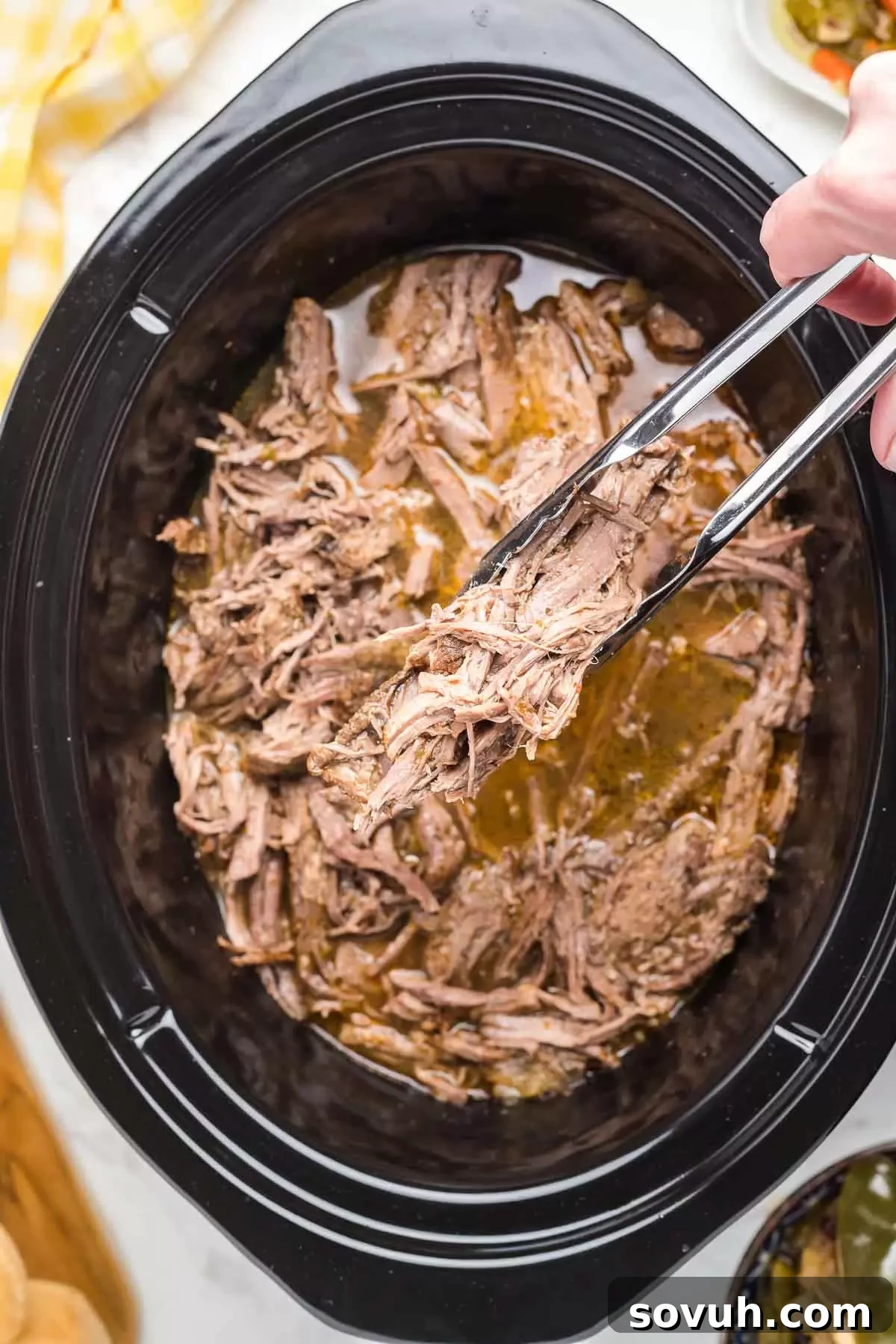 Serving Crock Pot Italian Beef from a slow cooker with tongs, showing tender shredded beef.