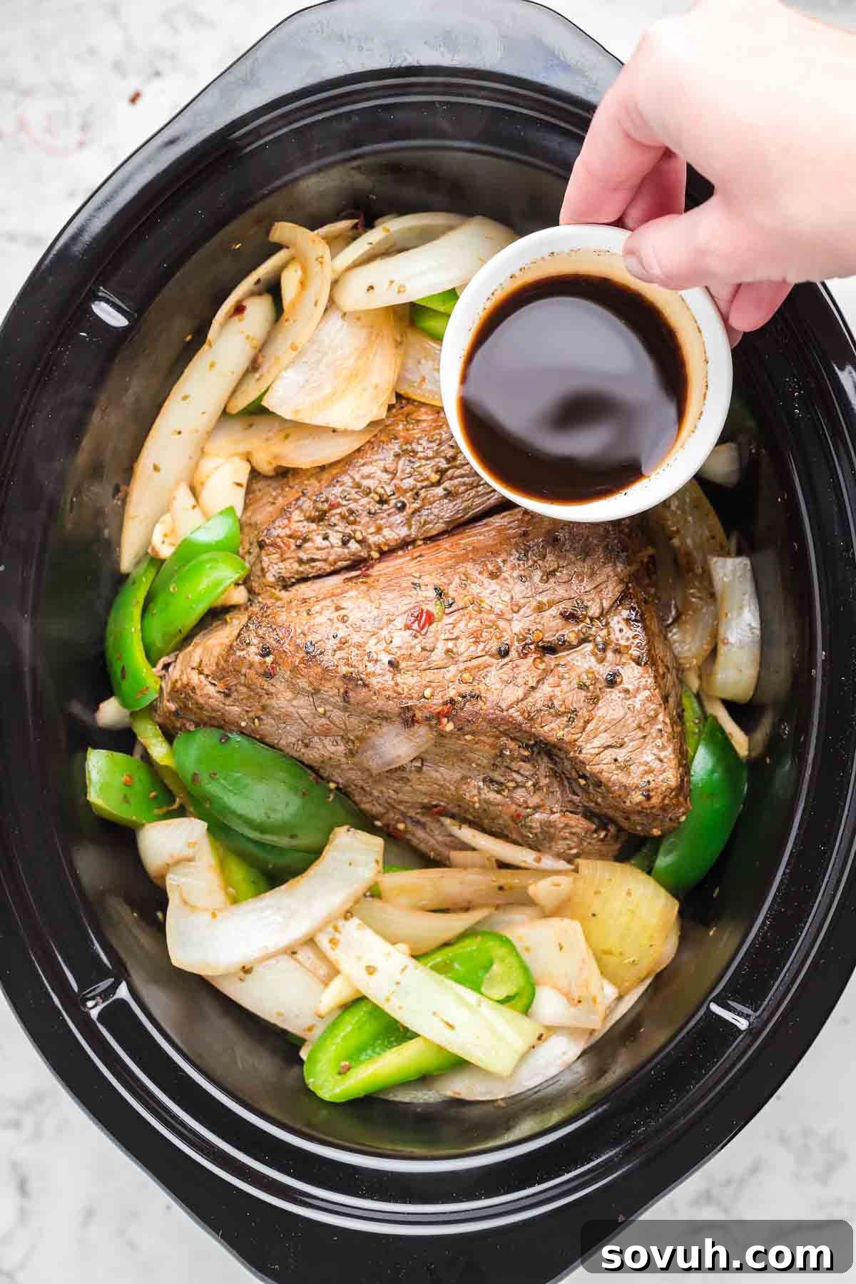 Pouring sauce over Crock Pot Italian Beef in a slow cooker.